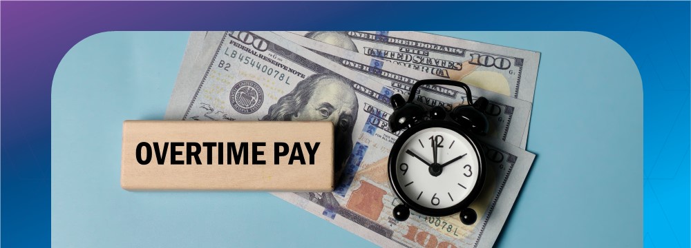 Overtime Pay written on a wooden block next to a black alarm clock sitting on 100 dollar bills